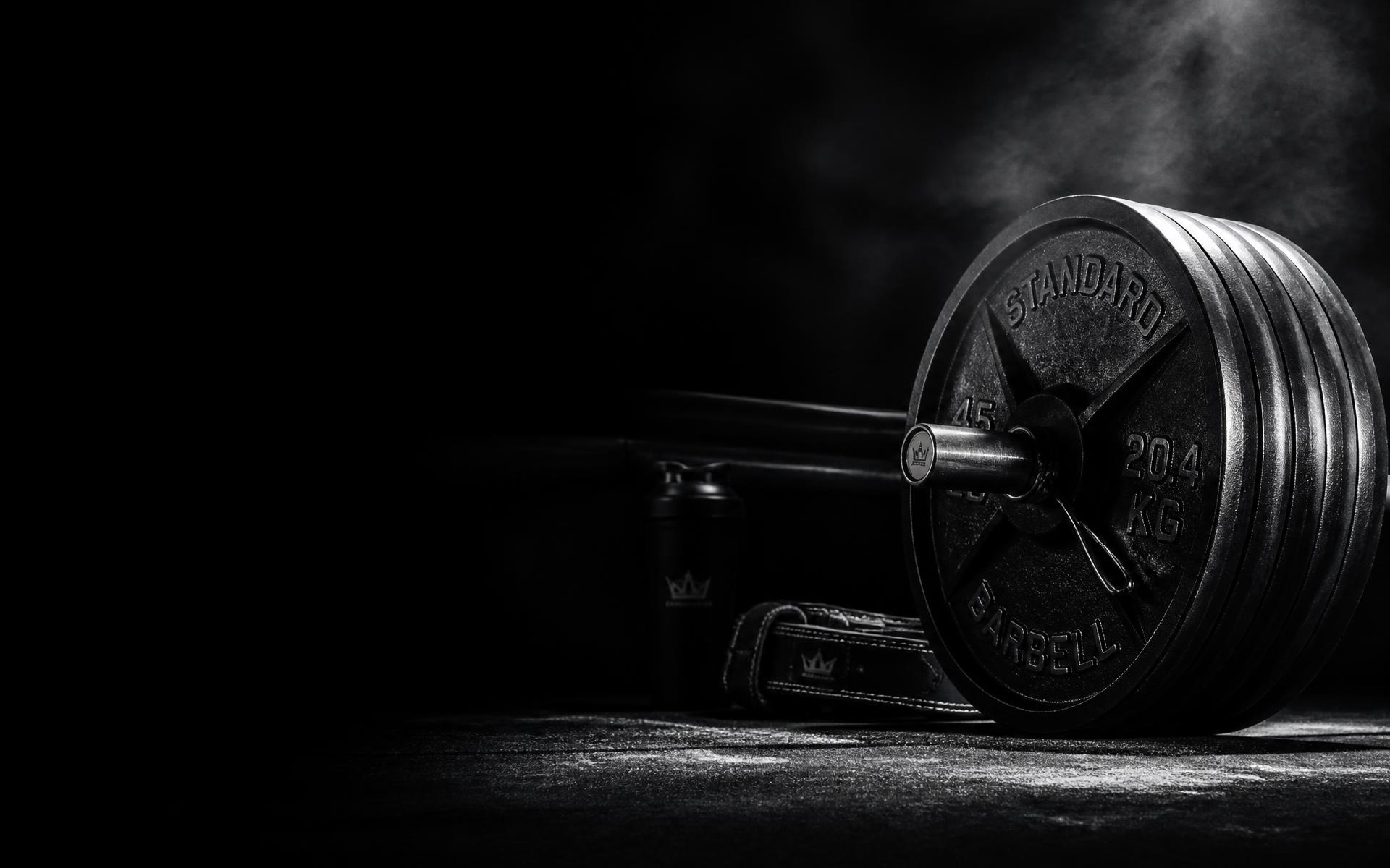 Barra olímpica y discos de acero en un gimnasio oscuro con iluminación lateral